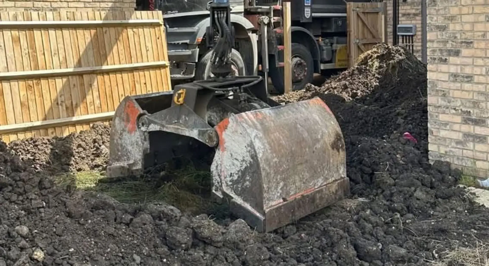 Grab bucket lifting excavated soil from a garden into a Sandy Grab Services lorry