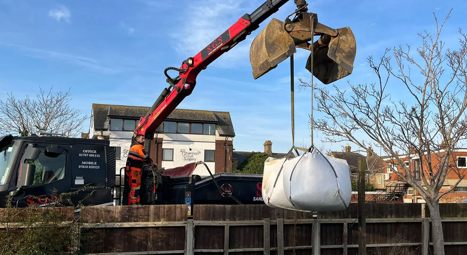 Sandy Grab Services grab lorry lifting a bulk bag over a garden fence